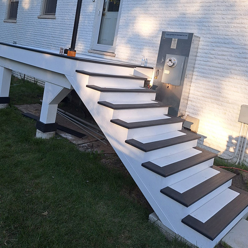Unas escaleras exteriores blancas con escalones de color marrón oscuro conducen a una casa con una pared texturizada, una puerta y una caja de medidor eléctrico.